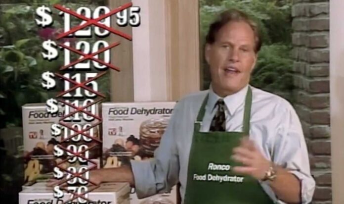 Ron Popeil apron stands next to a stack of food dehydrator boxes. A list of crossed-out prices appears on the left, showcasing a decreasing price promotion, ending with $10. The background has greenery visible through a window.