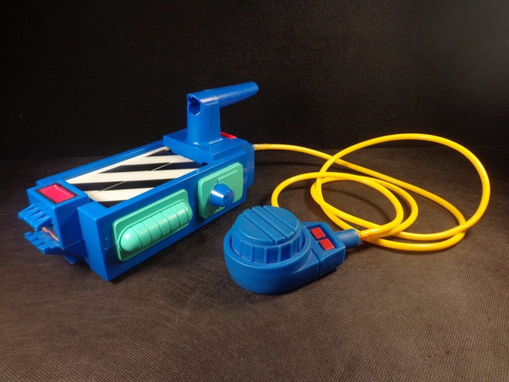 A blue vintage toy reminiscent of those used by the Ghostbusters, resembling a walkie-talkie with a long yellow cord attached to a round blue speaker. The device features various buttons and dials, displayed against a dark background.