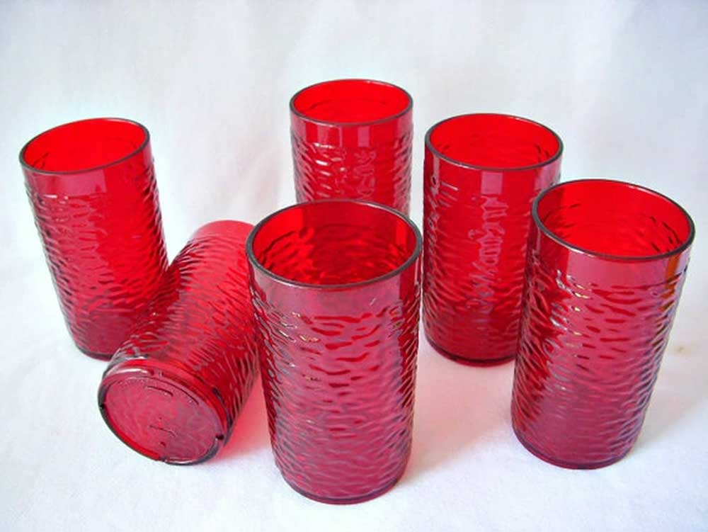 Five red textured glass tumblers are artfully arranged like a Pizza Hut setting, with one lying horizontally while the others stand upright on a pristine white surface.