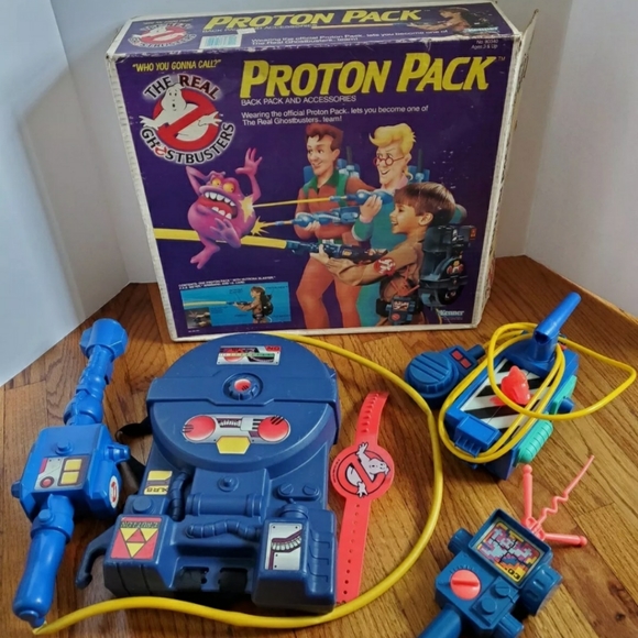 A vintage Proton Pack toy set from The Real Ghostbusters series, perfect for Ghostbusters Collectibles enthusiasts. The box features cartoon characters and a purple ghost. Inside, find wearable gear and a blue proton blaster with various buttons and controls.