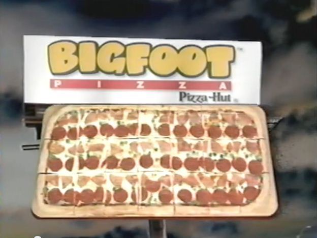 A large rectangular pizza topped with pepperoni is displayed on a wooden board, its irresistible aroma wafting through the air. Above it hangs a sign boldly proclaiming "Bigfoot Pizza" from Pizza Hut, set against the backdrop of a cloudy sky.