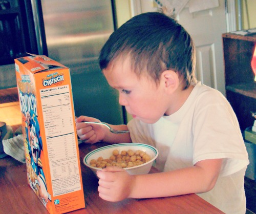 Kid eating peanut butter crunch cereal and staring at the back of the box