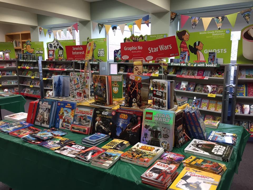 A colorful bookstore display featuring Star Wars books and graphic novels. The table is filled with various titles, with banners above indicating sections for Jewish interest and graphic novels. Shelves in the background hold more books.