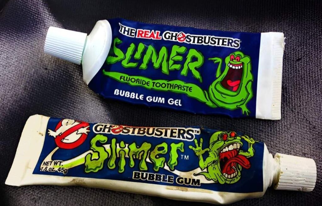 Two tubes of Ghostbusters-themed collectibles: the top one is Slimer fluoride toothpaste with bubble gum gel flavor, and the bottom one is Slimer bubble gum, both featuring green ghost illustrations.