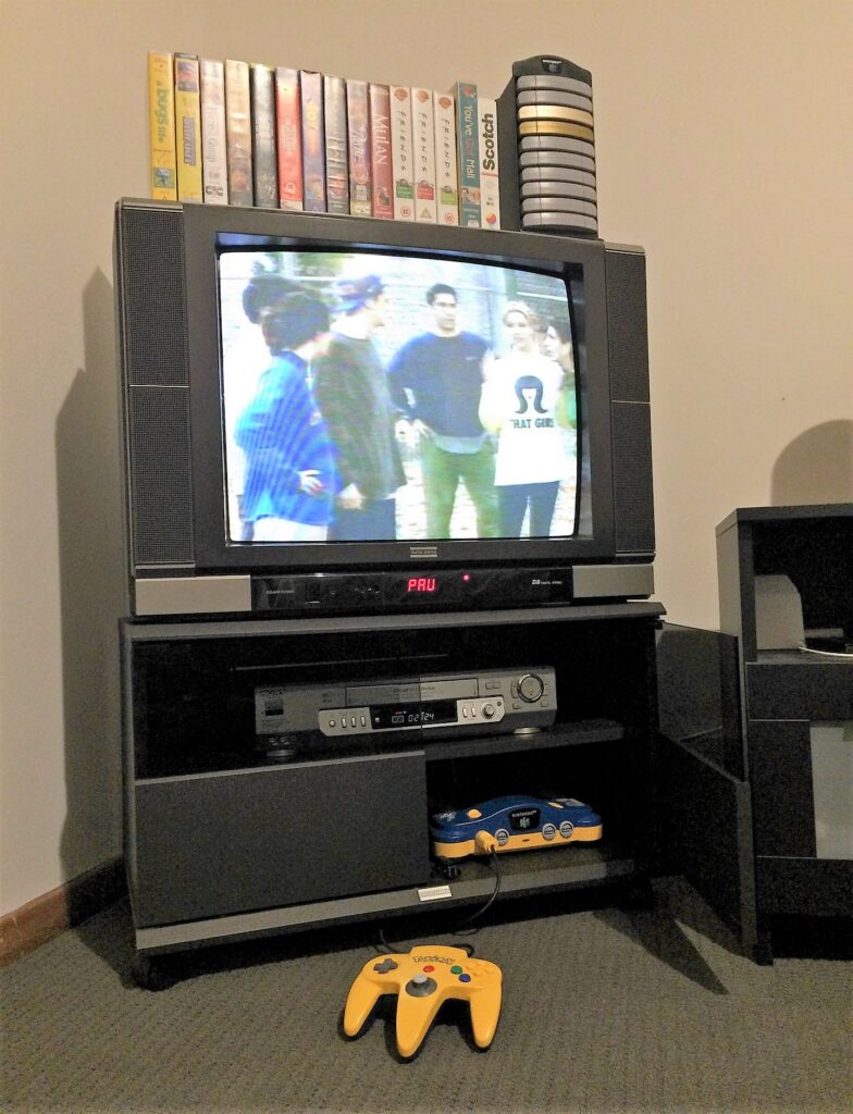 TV and VCR and Nintendo 64 with a collection of VHS tapes and the tv show Friends on TV. 