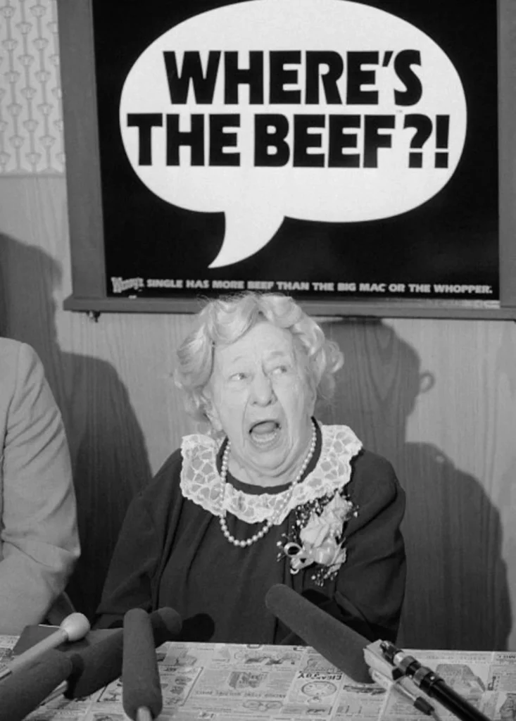 Clara Pellar sitting under a sign that says "Where's the beef?"