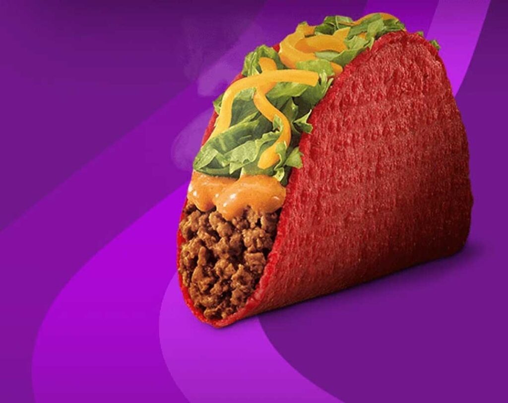 Discontinued fast food item - Taco Bell Volcano Taco. The vibrant red-shelled taco, reminiscent of beloved discontinued fast food items, is packed with seasoned ground beef and topped with shredded lettuce, cheddar cheese, and a dollop of sauce. It stands out against a purple background.