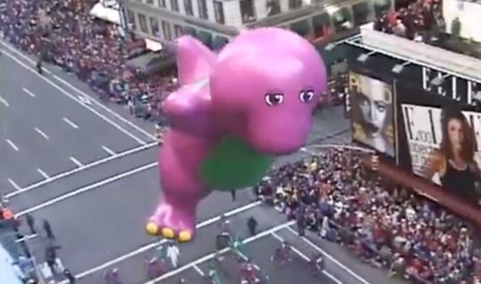 Barney Deflated at Macy's Day Parade - A large purple dinosaur balloon, reminiscent of the Barney balloon incident, floats above a crowded city street during a parade. The dinosaur has a green belly and pink feet. Spectators line the street, watching from sidewalks and nearby buildings, much like Macy’s Thanksgiving Day Parade.