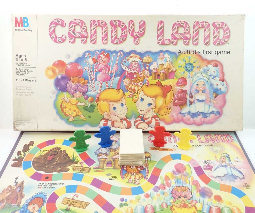 The image shows the Candy Land board game. The board is colorful, featuring a winding path with various candy-themed illustrations. Four colored player pieces (red, blue, yellow, green) are in front of the games box.