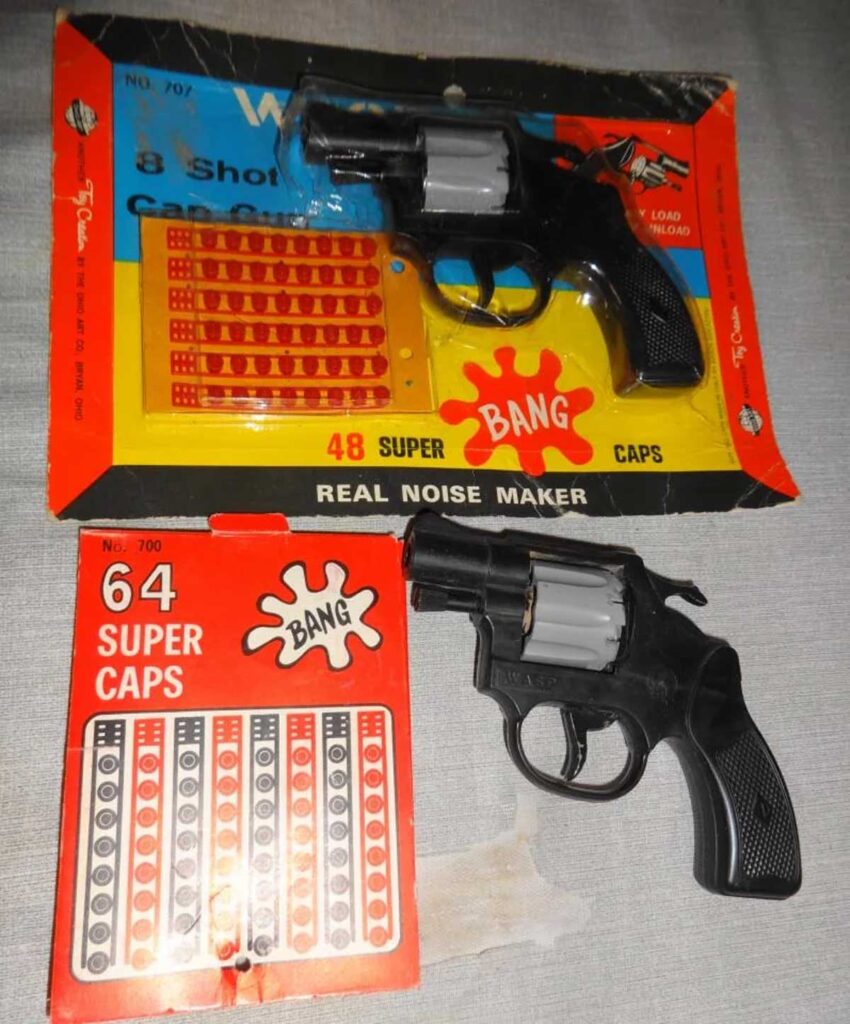 The image shows two toy revolver cap guns and their packaging. One package is orange with 48 Super Caps, and the other red with 64 Super Caps. Both display images of the caps with circular patterns, and the word Bang in bold letters.