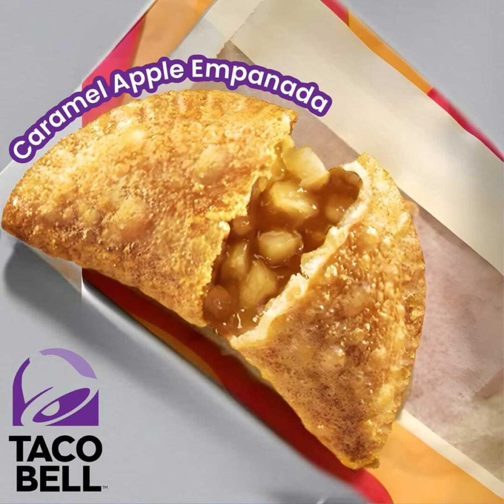 A close-up of a golden-brown caramel apple empanada with a crispy crust. It's cut open to reveal a filling of diced apples and caramel, a sweet reminder of discontinued Taco Bell menu items. The Taco Bell logo is visible in the bottom left corner.