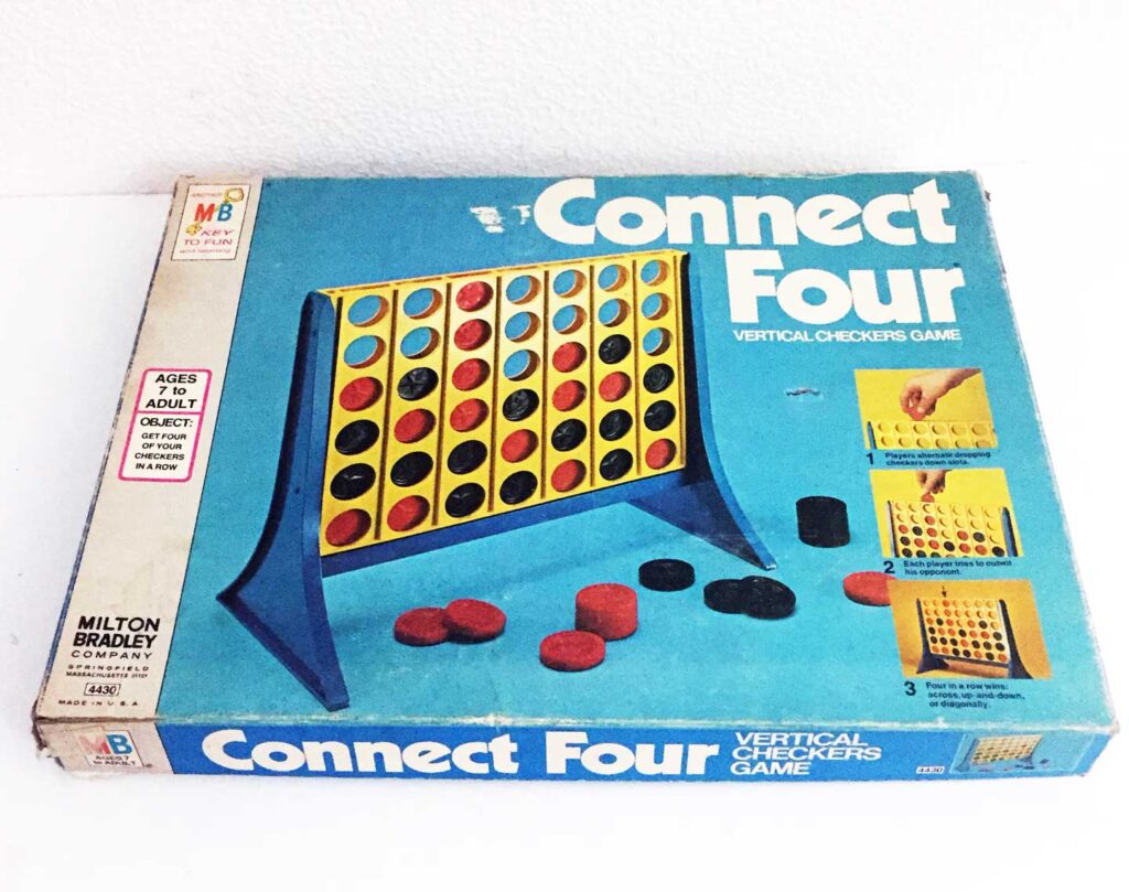 A vintage Connect Four game box features an illustration of the game board set up with red and black discs. The box is blue with white text. Its labeled for ages 7 to adult and highlights being a vertical checkers game.