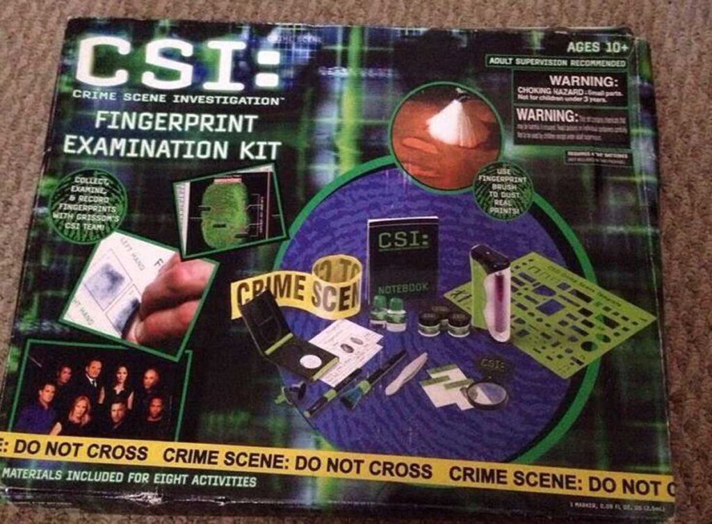 Image of a CSI: Crime Scene Investigation Fingerprint Examination Kit box. Includes items like a notebook, magnifying glass, test tubes, and crime scene tape, for ages 10 and up. Contains warnings and supervision recommendations.