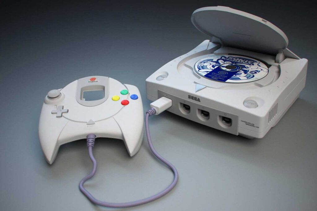 A Sega Dreamcast console, one of the best-selling video game consoles, has its lid open to reveal a Sonic Adventure disc. Next to it, a white controller with a small screen and colorful buttons rests on the flat surface.