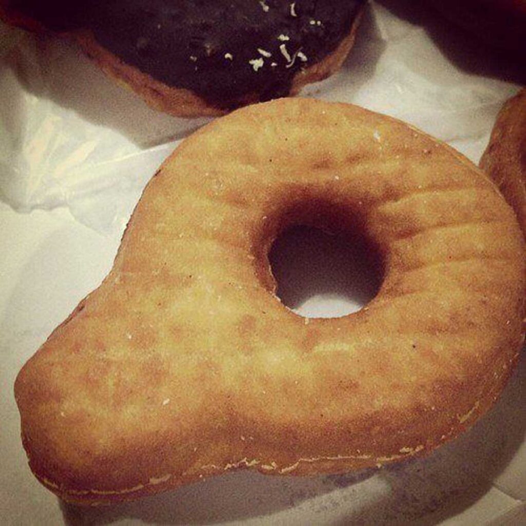 A close-up of a golden-brown doughnut shaped like a light bulb, reminiscent of discontinued fast food items, with a traditional hole in the center, placed on a light surface.