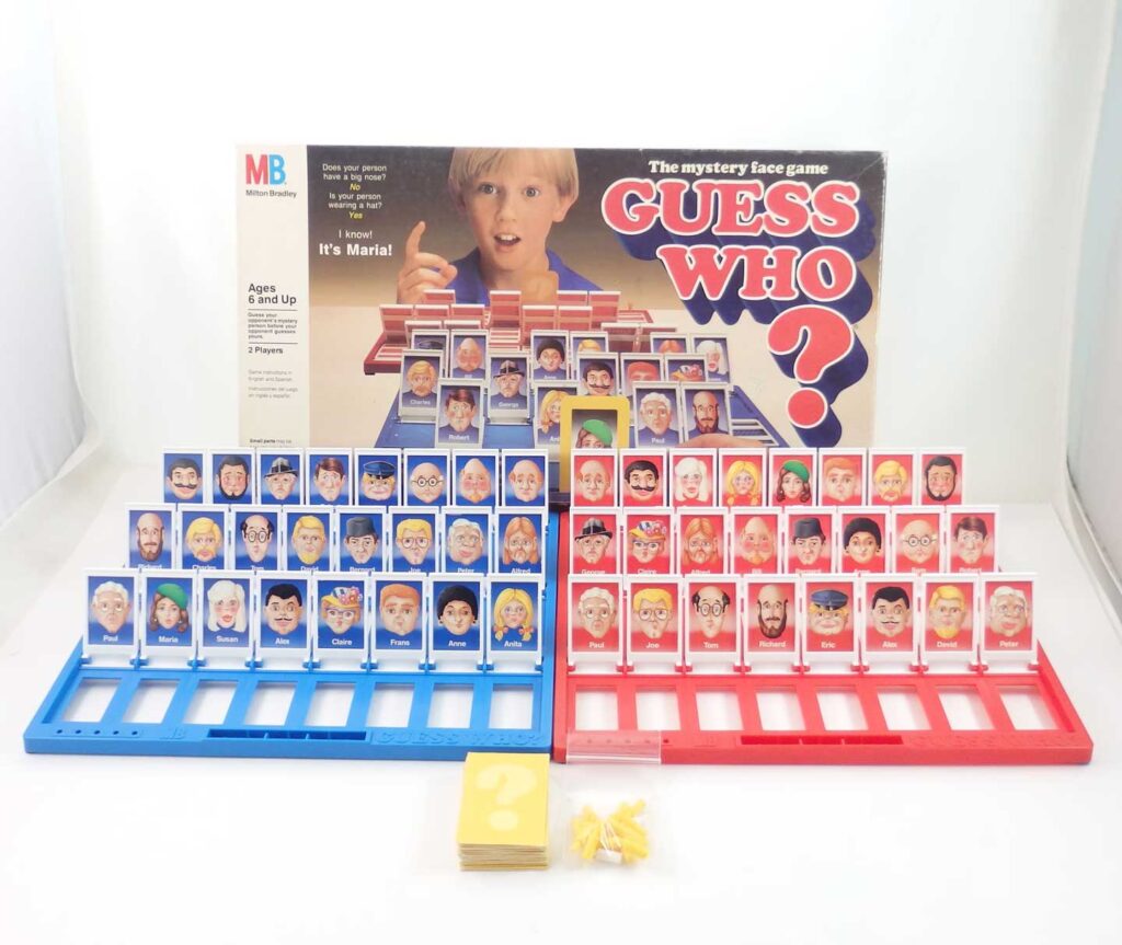 A vintage Guess Who? board game set featuring two boards with character cards, blue and red, laid out in front of the box. The box showcases the games logo and a child playing.