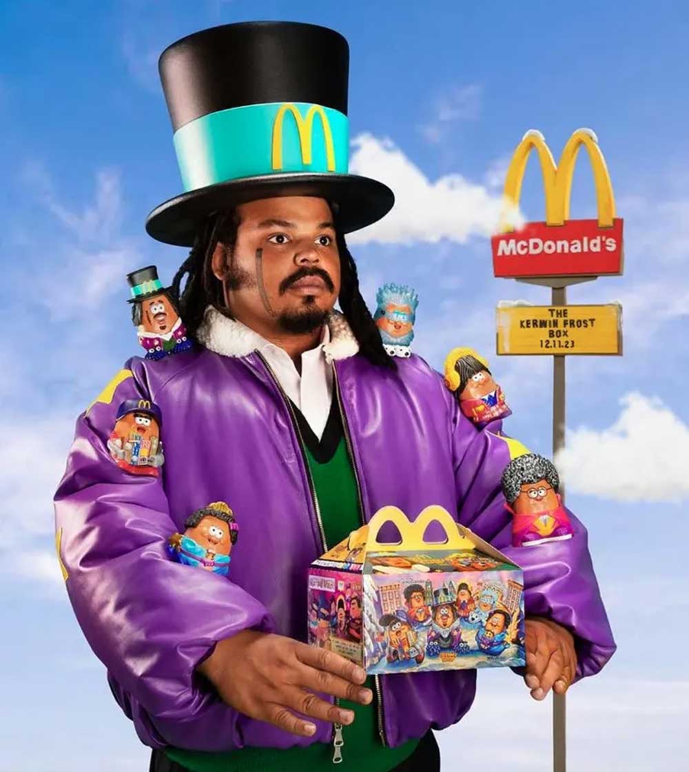 A man in a large top hat and a purple jacket holds a McDonalds Happy Meal box, with McDonalds-themed toys attached to his clothing. A McDonalds sign and a blue sky are in the background.