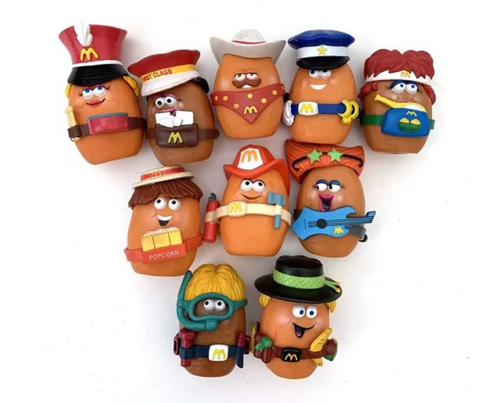 A collection of toy figures resembling potatoes, each dressed in a unique costume, including a firefighter, cowboy, pilot, musician, and more. The toys are arranged in a triangle shape on a white background.