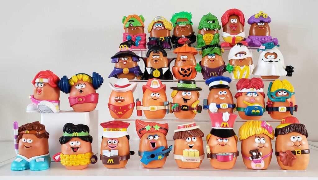 A collection of McNugget Buddies, each dressed in costumes like superheroes, royalty, and athletes, arranged on a shelf. Bright colors and playful expressions give each figure a unique personality.