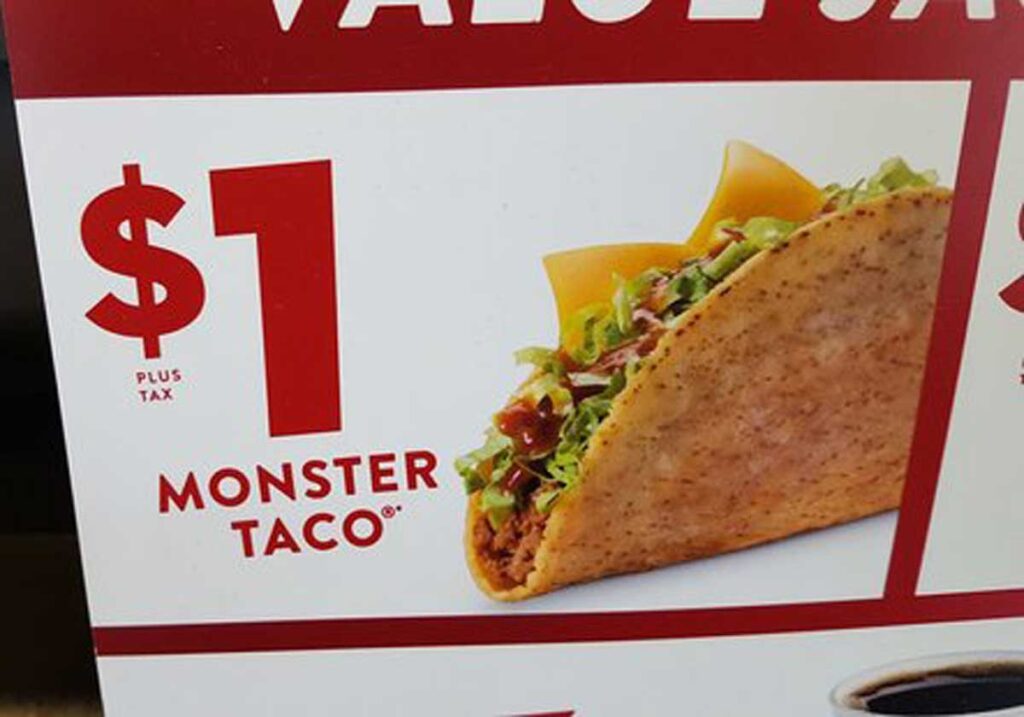 Close-up of a food advertisement showcasing the discontinued fast food item, a taco with cheese, lettuce, and sauce. Next to the tasty taco, bold text reads: $1 PLUS TAX MONSTER TACO.