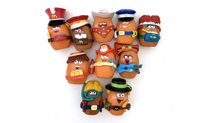 Most Iconic Happy Meals Toys - A collection of ten McNugget Buddies Happy Meal toys, each dressed in unique costumes, including a firefighter, cowboy, pirate, and others. They are arranged in two rows against a white background.