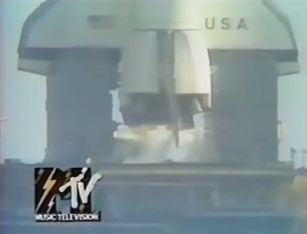 MTV's first broadcast - A rocket labeled USA is launching, with visible flames and smoke at its base, reminiscent of the excitement surrounding MTV's first broadcast. The MTV Music Television logo is displayed in the bottom left corner.