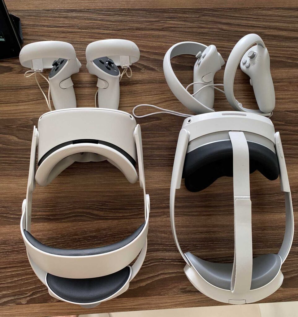 Two white virtual reality headsets, inspired by the best-selling video game consoles, with matching controllers rest on a wooden surface. The headsets have straps and padded interiors, and the controllers are positioned beside them, each pair connected with a charging cable.