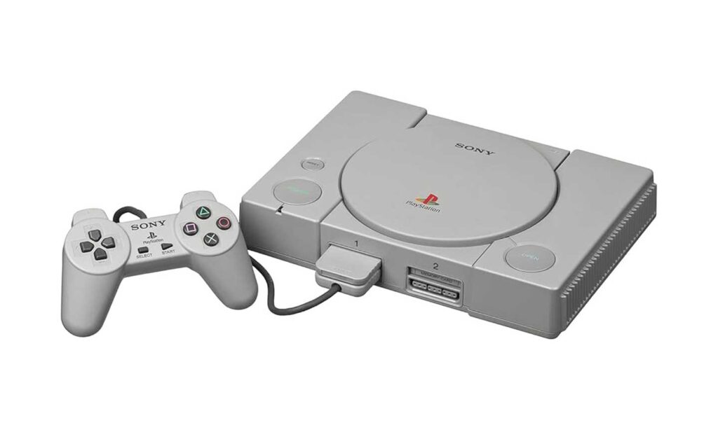 A grey Sony PlayStation console, one of the best-selling video game consoles, includes a matching wired controller. The console features the iconic PlayStation logo and has two controller ports on the front. The controller comes equipped with a directional pad, buttons, and two joysticks.