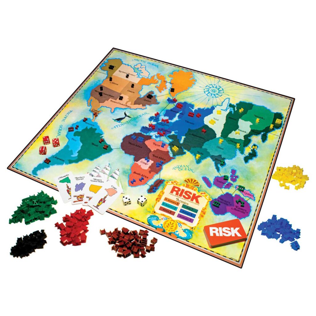 Image of the board game Risk. The game board features a world map with colored territories. Nearby are dice, game cards, and piles of small army pieces in various colors, including red, green, black, yellow, and blue.