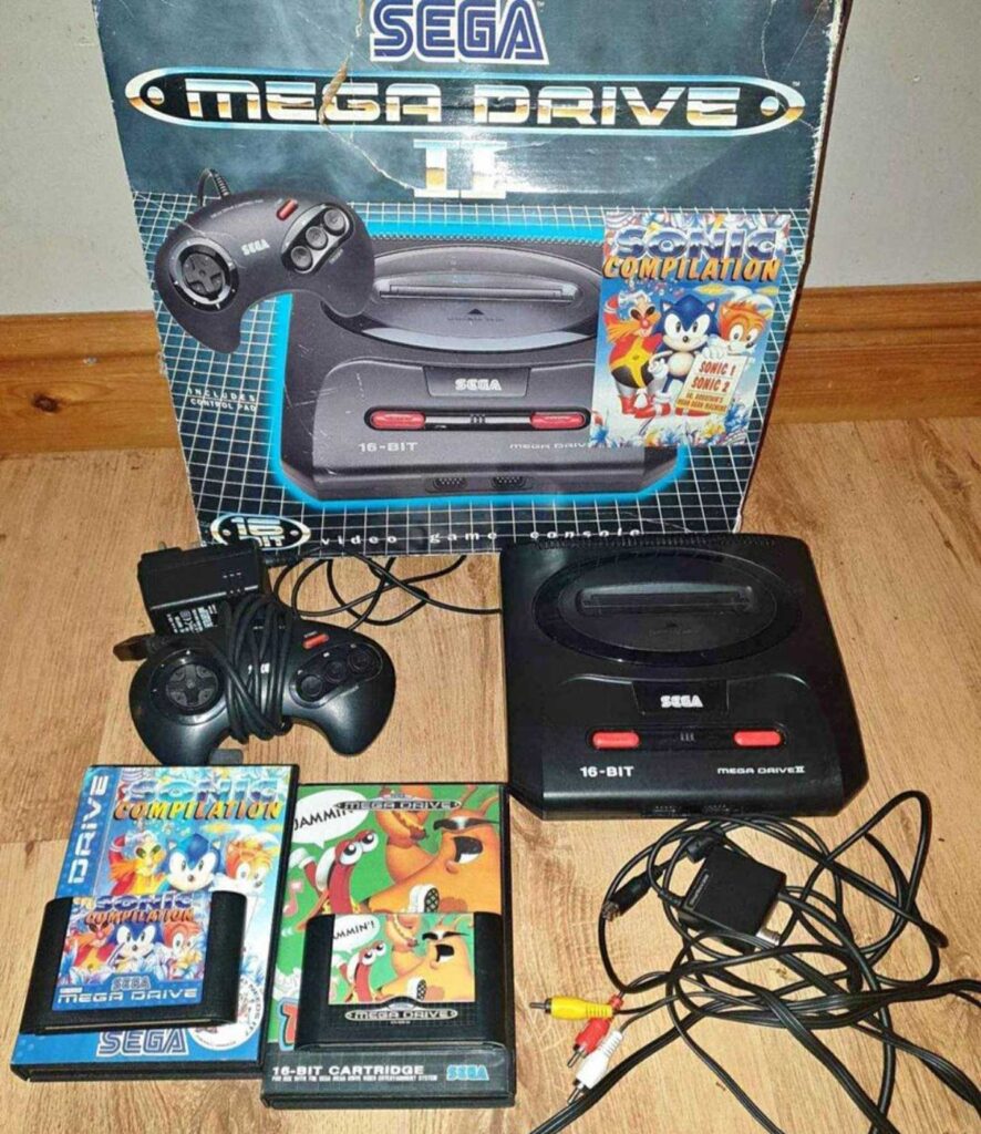 A Sega Mega Drive 16-bit console set with two controllers, a power adapter, AV cables, and three game cartridges. Among the best-selling video game consoles of its time, it comes complete with original packaging in the background and game covers featuring colorful illustrations.