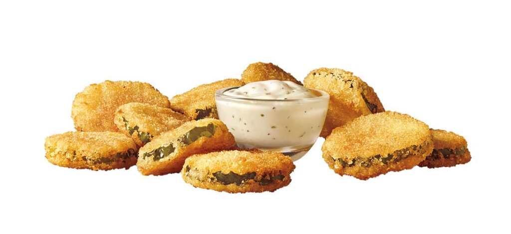 A group of breaded, fried pickles reminiscent of discontinued fast food items is arranged around a small glass bowl of creamy dipping sauce on a white background.