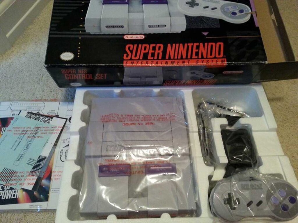 A Super Nintendo Entertainment System (SNES), one of the best-selling video game consoles, is displayed in its original packaging. The box, console, controller, and components are neatly arranged in foam. An instruction manual and promotional inserts are partially visible to the side.