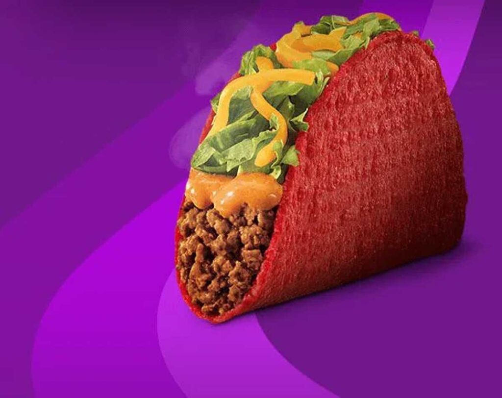 A vibrant red taco shell, reminiscent of discontinued Taco Bell menu items, filled with seasoned ground beef, topped with melted cheese sauce, shredded cheddar cheese, and fresh lettuce, placed against a purple background.