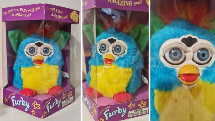 A colorful Furby toy is displayed in its packaging, featuring blue, yellow, and green fur with big eyes. The box has vibrant purple text saying, The more you play with me, the more I do! I will keep amazing you!.