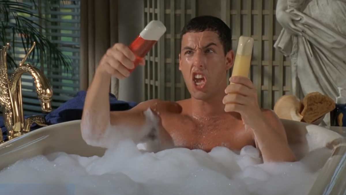 Adam Sandler as Billy Madison in a bubble bath holding two brightly colored bottles with humorous expressions. The bathroom is elaborately decorated with plants and a golden tap.