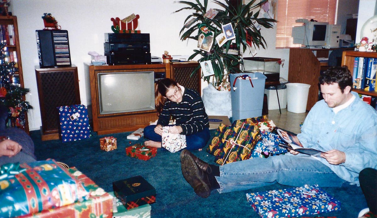 Christmas morning in the 90s, unwrapping presents. In the background a 90s desktop computer can be seen. 