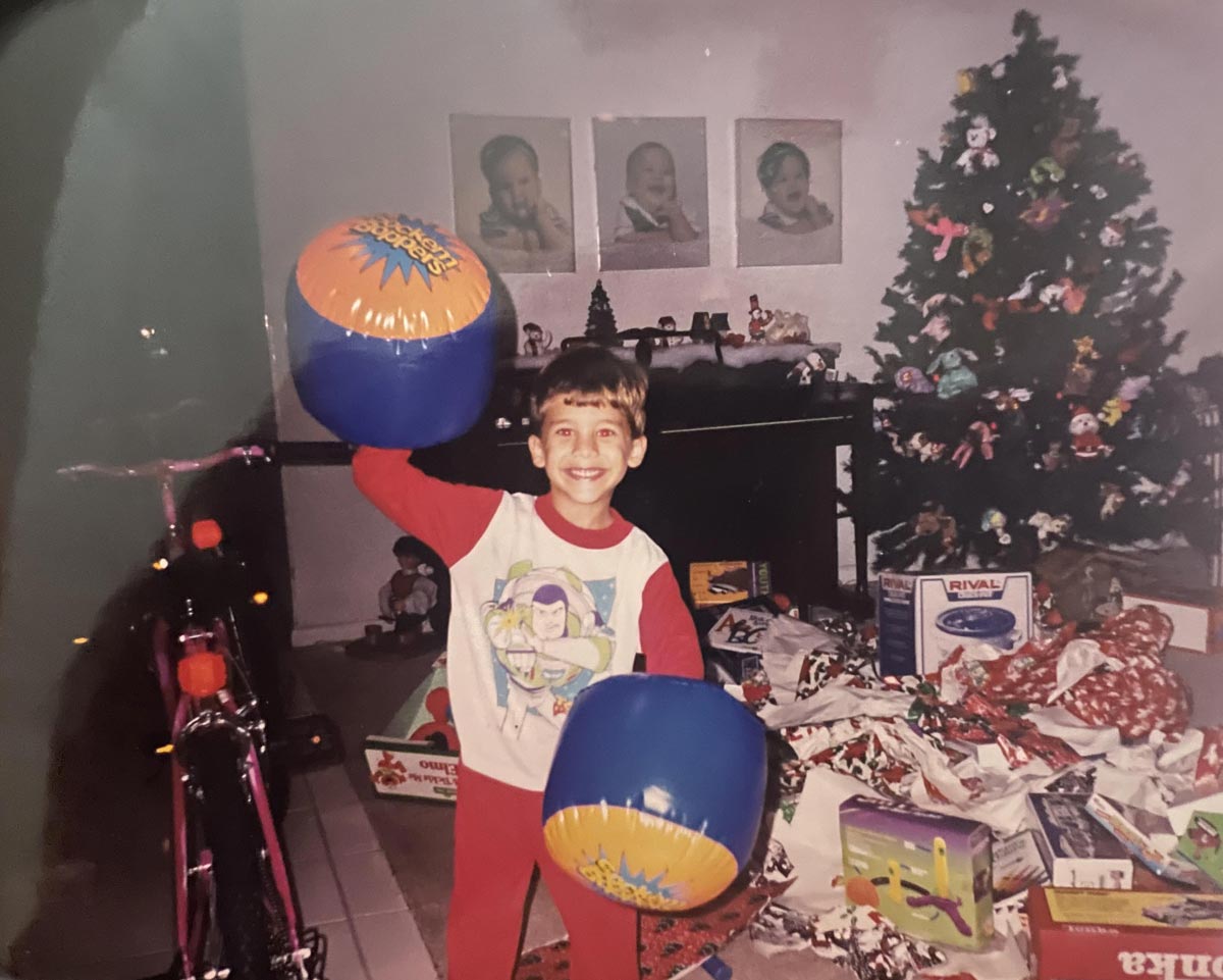 Kid on Christmas morning surrounded by presents and behind him is a Christmas tree decorated with Beanie Babies