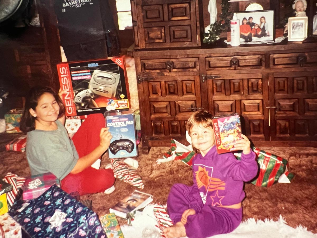 Two kids on Christmas morning holding a Sega Genesis, controller, and a game. A VHS copy of Free Willy is on the ground.