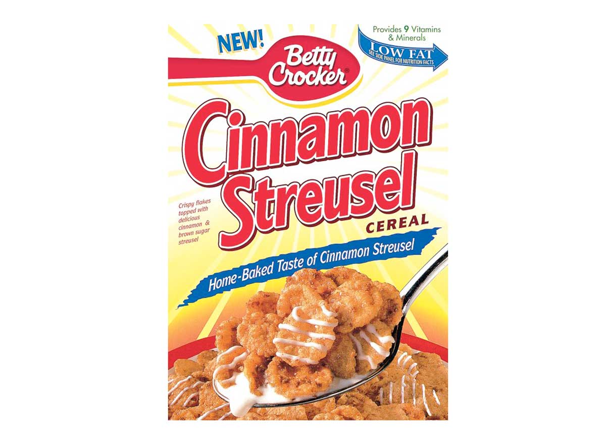 A box of the discontinued breakfast cereal, Betty Crocker Cinnamon Streusel. The front features a spoon with cereal topped with icing. Text highlights its low-fat content and vitamins. Bright red and yellow colors with a background sunburst pattern add to its nostalgic charm.