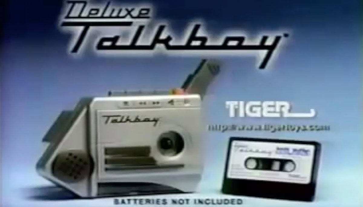 Image of a Deluxe Talkboy cassette player with an audio cassette beside it. The background is blue and features the text Deluxe Talkboy and Tiger. The phrase Batteries not included is shown at the bottom.