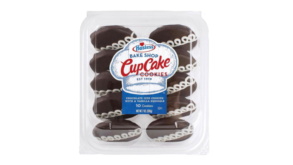 A clear plastic container holds ten Hostess Bake Shop CupCake Cookies. The cookies are chocolate iced with white vanilla squiggles on top. The packaging label is blue and white with red accents.