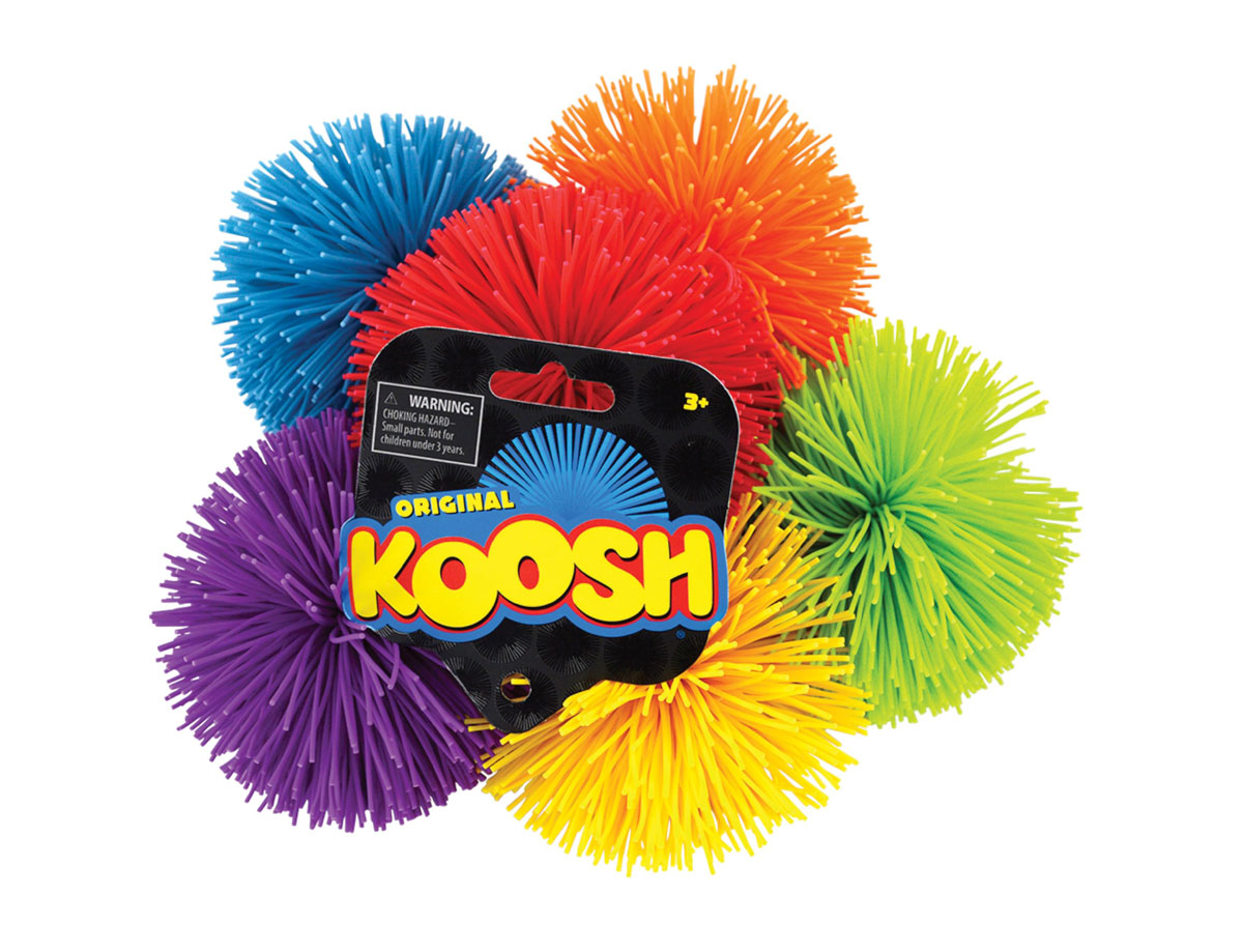 A group of colorful Koosh balls in blue, pink, orange, green, purple, and yellow. A black tag is attached, displaying Original Koosh and a warning label. The balls have soft, rubbery spikes.