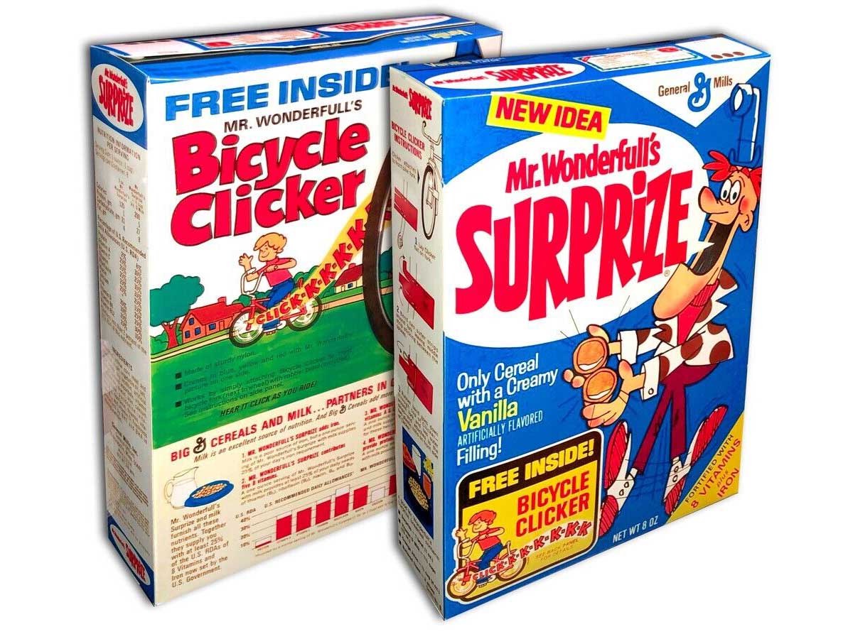 Front and back of a cereal boxes of Mr. Wonderful’s Surprize, featuring colorful graphics and cartoon characters. One box highlights a Bicycle Clicker toy offer. Both boxes boast vibrant designs and promotional text about the creamy vanilla-filled cereal.