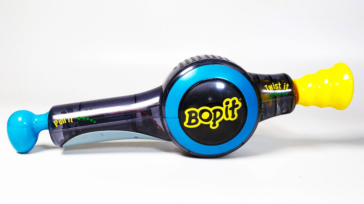 A Bop It toy with a black body, blue accents, and yellow ends. The center reads Bop It in yellow letters, and the ends are labeled Pull It and Twist It. The toy is on a white background.