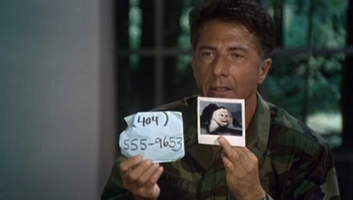 A man in military attire holds up a Polaroid photo of a monkey and a piece of paper with the phone number (404) 555-9653 written on it. The background shows a window and greenery outside.