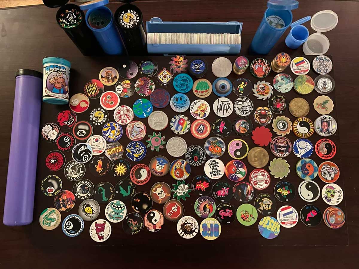 A collection of colorful pogs featuring various designs, such as yin-yang symbols, cartoon characters, and geometric patterns, is displayed on a table. Containers for storage are placed around the pogs.