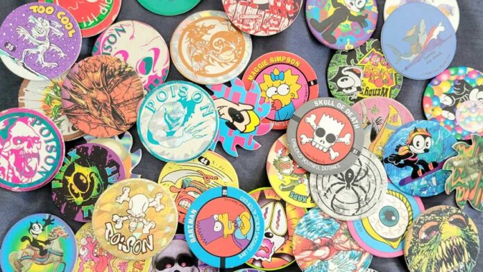 A collection of colorful pogs scattered on a surface, featuring various designs including cartoon characters, skulls, and abstract patterns. Some prominent colors are bright pink, yellow, and blue.