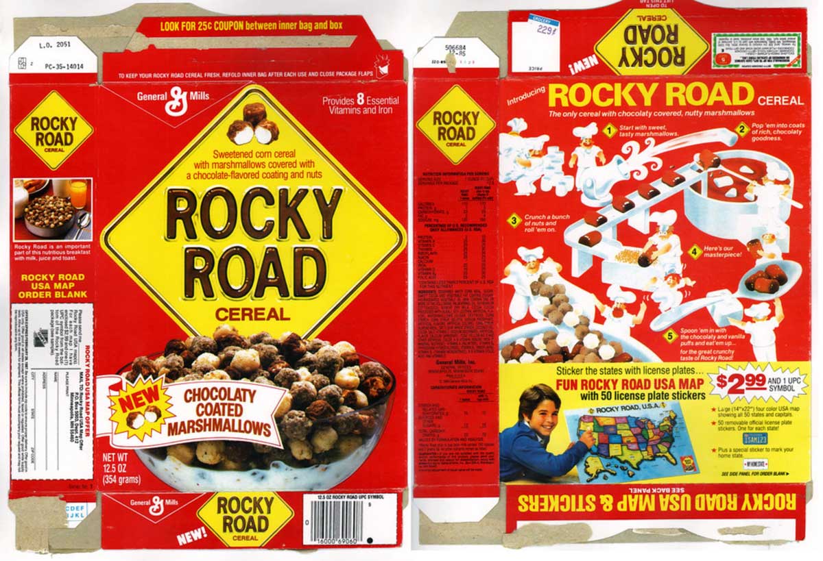 A colorful cereal box for Rocky Road Cereal featuring chocolaty coated marshmallows. The front displays a bowl of cereal, while the back has puzzles and games for kids. Bright red background with a yellow diamond logo. Includes promotional offers.