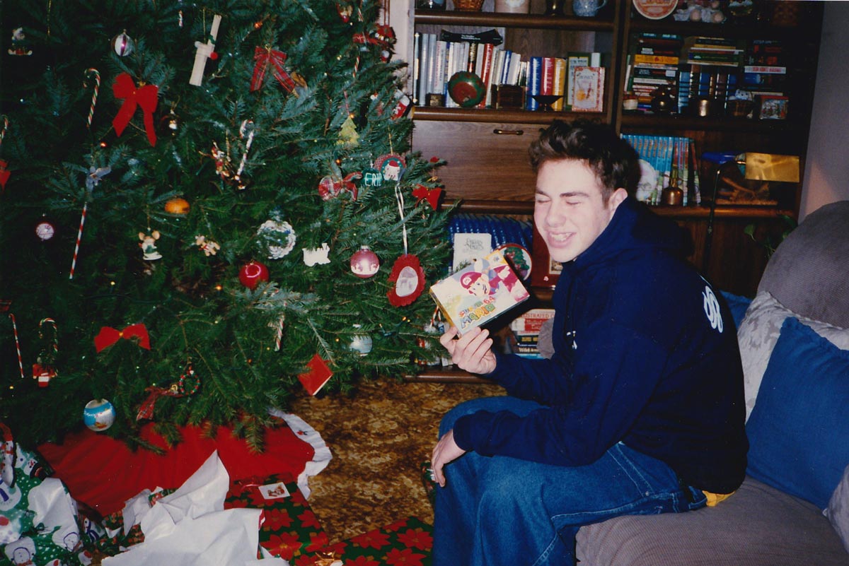 Christmas morning and a teen holding up a Super Mario 64 game he got for Christmas