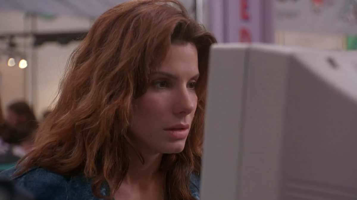 A person with long brown hair is intently looking at a computer monitor. The setting appears to be indoors with blurred background elements.